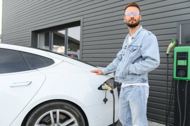 Bir adam elektrikli arabayı şarj eder..