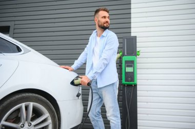 Şık bir adam elektrikli araba şarj prizine takar..