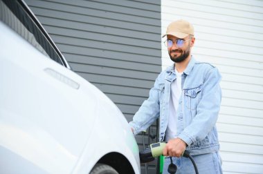 Şık bir adam elektrikli araba şarj prizine takar..