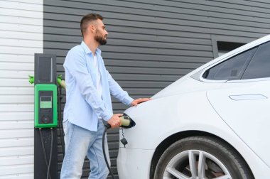 Güzel, genç, şık bir adam, gündüz vakti elektrikli arabasıyla aracı şarj ediyor..