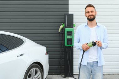 Bir adam elektrikli arabayı şarj eder..