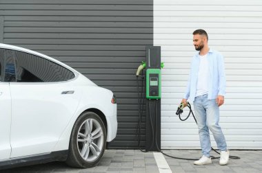 Bir adam elektrikli arabayı şarj eder..