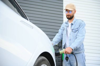Güzel, genç, şık bir adam, gündüz vakti elektrikli arabasıyla aracı şarj ediyor..