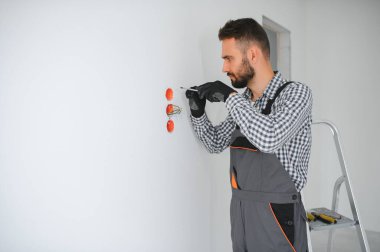 Elektrik İmalathanesi, prizler ve şalter kurulumu. Elektrikçi aletli profesyonel bir işçi. Tamir alanının arka planına karşı.