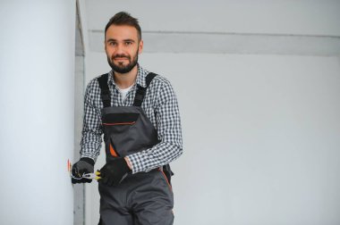 Elektrik İmalathanesi, prizler ve şalter kurulumu. Elektrikçi aletli profesyonel bir işçi. Tamir alanının arka planına karşı.