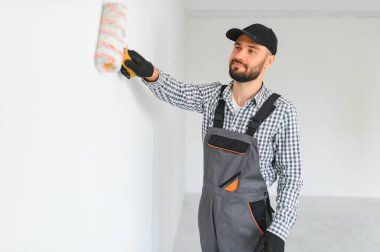 Üniformalı genç profesyonel işçi boya silindiriyle ayakta duruyor.