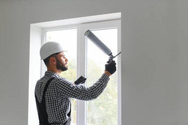 Silikon tabanca ile yapıştırıcı uygulayarak genç bir erkek işçi yan görünüm.