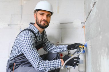 Gri kanalizasyon borularıyla çalışan genç tesisatçının yatay görüntüsü tornavidayla duvara sabitleniyor.