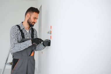 Üniformalı elektrikçi beyaz duvara elektrik prizleri takıyor..