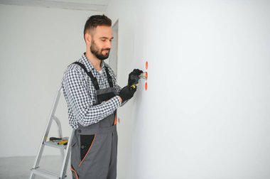 Elektrik İmalathanesi, prizler ve şalter kurulumu. Elektrikçi aletli profesyonel bir işçi. Tamir alanının arka planına karşı.