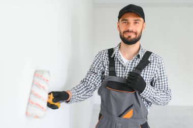 Üniformalı genç profesyonel işçi boya silindiriyle ayakta duruyor.