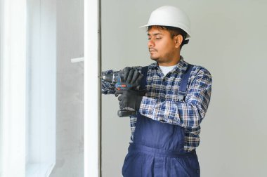 Hintli İşçi tulumlu, evdeki oturma odasına plastik pencereler yerleştiriyor ya da ayarlıyor.