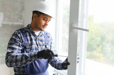 Hintli İşçi tulumlu, evdeki oturma odasına plastik pencereler yerleştiriyor ya da ayarlıyor.