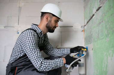 Gri kanalizasyon borularıyla çalışan genç tesisatçının yatay görüntüsü tornavidayla duvara sabitleniyor.