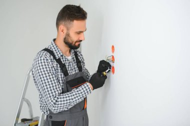 Ciddi erkek elektrikçi daireye priz yerleştiriyor ve tornavida kullanıyor..