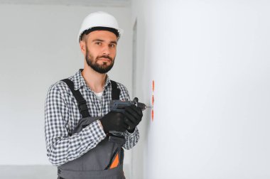 Elektrik İmalathanesi, prizler ve şalter kurulumu. Elektrikçi aletli profesyonel bir işçi. Tamir alanının arka planına karşı.