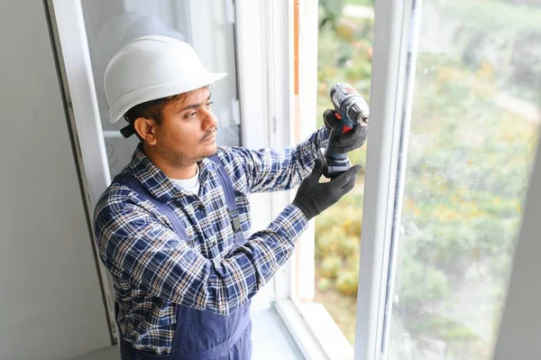 自宅のリビングルームにプラスチック窓を設置または調整するオーバーオールインインディアンワークマン — ストック写真