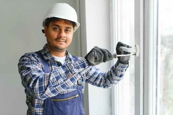 Indyjski Robotnik Kombinezonach Instalujący Lub Regulujący Plastikowe Okna Salonie Domu — Zdjęcie stockowe