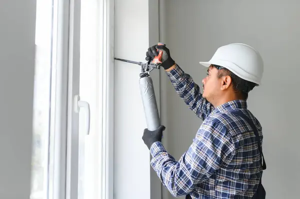 Indian worker using a silicone tube for repairing of window indoor.