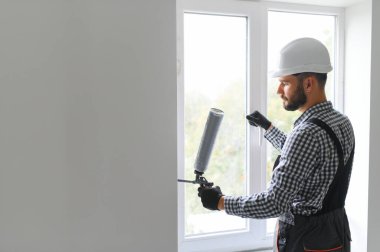 Silikon tabanca ile yapıştırıcı uygulayarak genç bir erkek işçi yan görünüm.