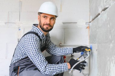 Gri kanalizasyon borularıyla çalışan genç tesisatçının yatay görüntüsü tornavidayla duvara sabitleniyor.