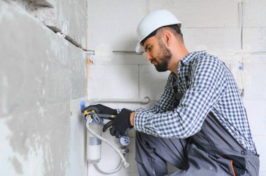 Gri kanalizasyon borularıyla çalışan genç tesisatçının yatay görüntüsü tornavidayla duvara sabitleniyor.