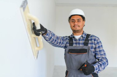 Hintli bir işçi boş bir dairede çalışıyor. Üniformalı bir adam binanın içinde tamirat yapıyor..