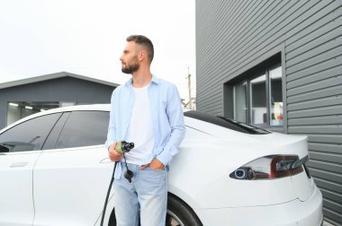 Evin yanında elektrikli araba şarj eden bir adam var.