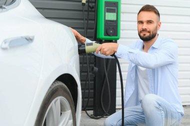 Bir adam elektrikli arabayı şarj eder..
