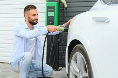 Şık bir adam elektrikli araba şarj prizine takar..