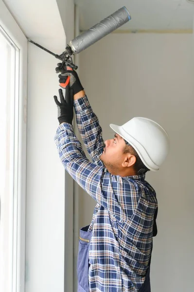 Indian worker using a silicone tube for repairing of window indoor.