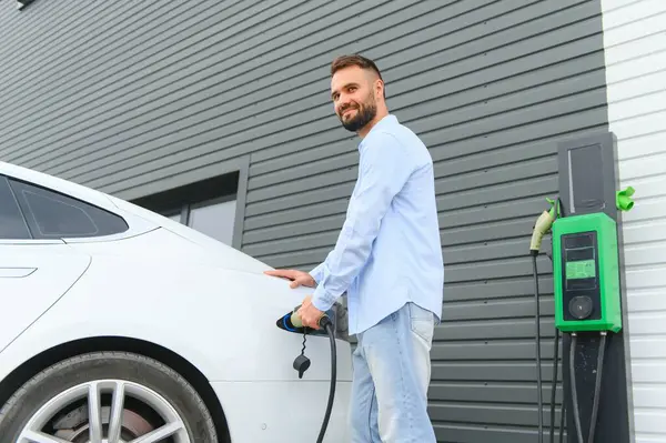 Şık bir adam elektrikli araba şarj prizine takar..