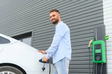 Güzel, genç, şık bir adam, gündüz vakti elektrikli arabasıyla aracı şarj ediyor..