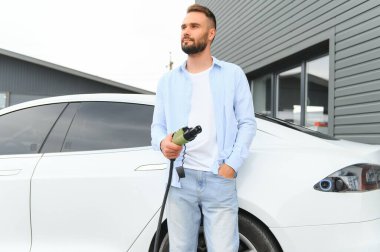 Güzel, genç, şık bir adam, gündüz vakti elektrikli arabasıyla aracı şarj ediyor..