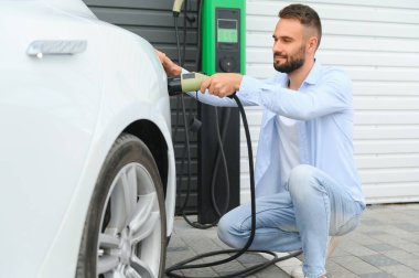 Şık bir adam elektrikli araba şarj prizine takar..