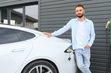Kalkıp şarjın bitmesini bekliyorlar. Genç şık adam, gündüz vakti elektrikli arabayla geziyor..