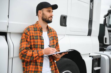 Dağıtım deposunun otoparkında dururken kamyon şoförü sevkiyat listesini kontrol ediyor.