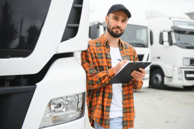 Dağıtım deposunun otoparkında dururken kamyon şoförü sevkiyat listesini kontrol ediyor.