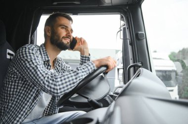 Genç profesyonel sürücü kamyon kullanırken cep telefonuyla iletişim kuruyor..