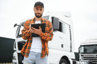 Dağıtım deposunun otoparkında dururken kamyon şoförü sevkiyat listesini kontrol ediyor.
