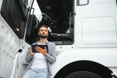Genç yakışıklı kamyon şoförü kamyonun yanında bir tabletle duruyor..
