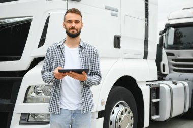 Genç yakışıklı kamyon şoförü kamyonun yanında bir tabletle duruyor..