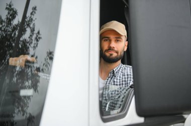 Kamyonun içinde oturan bir sürücü, arka planda birden fazla kamyonla açık pencereden içeri bakıyor..