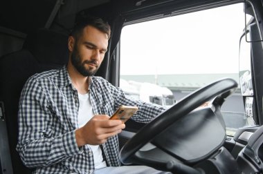 Genç profesyonel sürücü kamyon kullanırken cep telefonuyla iletişim kuruyor..