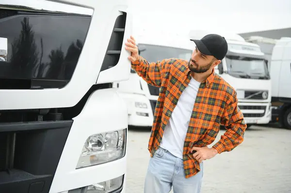 Portrait of young bearded trucker standing by his truck vehicle. Transportation service. Truck driver job.