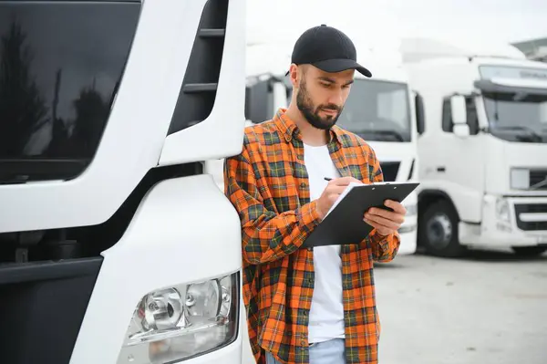 配送倉庫の駐車場に立っている間郵送物リストを点検するトラック運転手 ストック写真