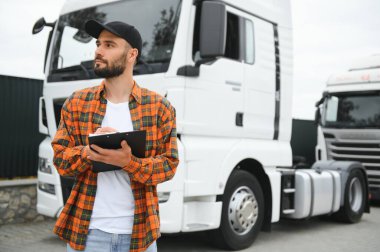 Dağıtım deposunun otoparkında dururken kamyon şoförü sevkiyat listesini kontrol ediyor.