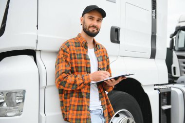 Dağıtım deposunun otoparkında dururken kamyon şoförü sevkiyat listesini kontrol ediyor.