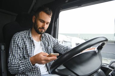 Genç profesyonel sürücü kamyon kullanırken cep telefonuyla iletişim kuruyor..