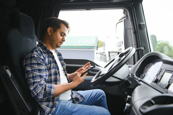 A young Indian male truck driver sits behind the wheel.